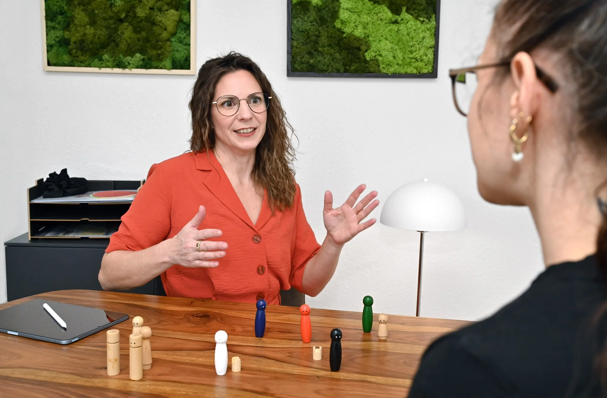 Scene einer Familienaufstellung mit Holzfiguren, Coach und Klientin sitzen am Tisch